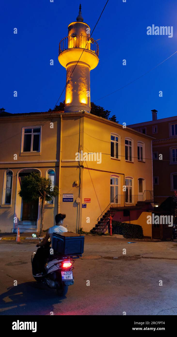 Livreur sur une moto la nuit dans une rue d'Istanbul Turquie avec un bâtiment et un minaret derrière. Banque D'Images