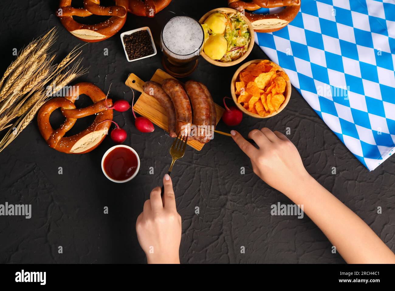 Femme mangeant de savoureuses saucisses bavaroises sur fond noir. Célébration de l'Oktoberfest Banque D'Images