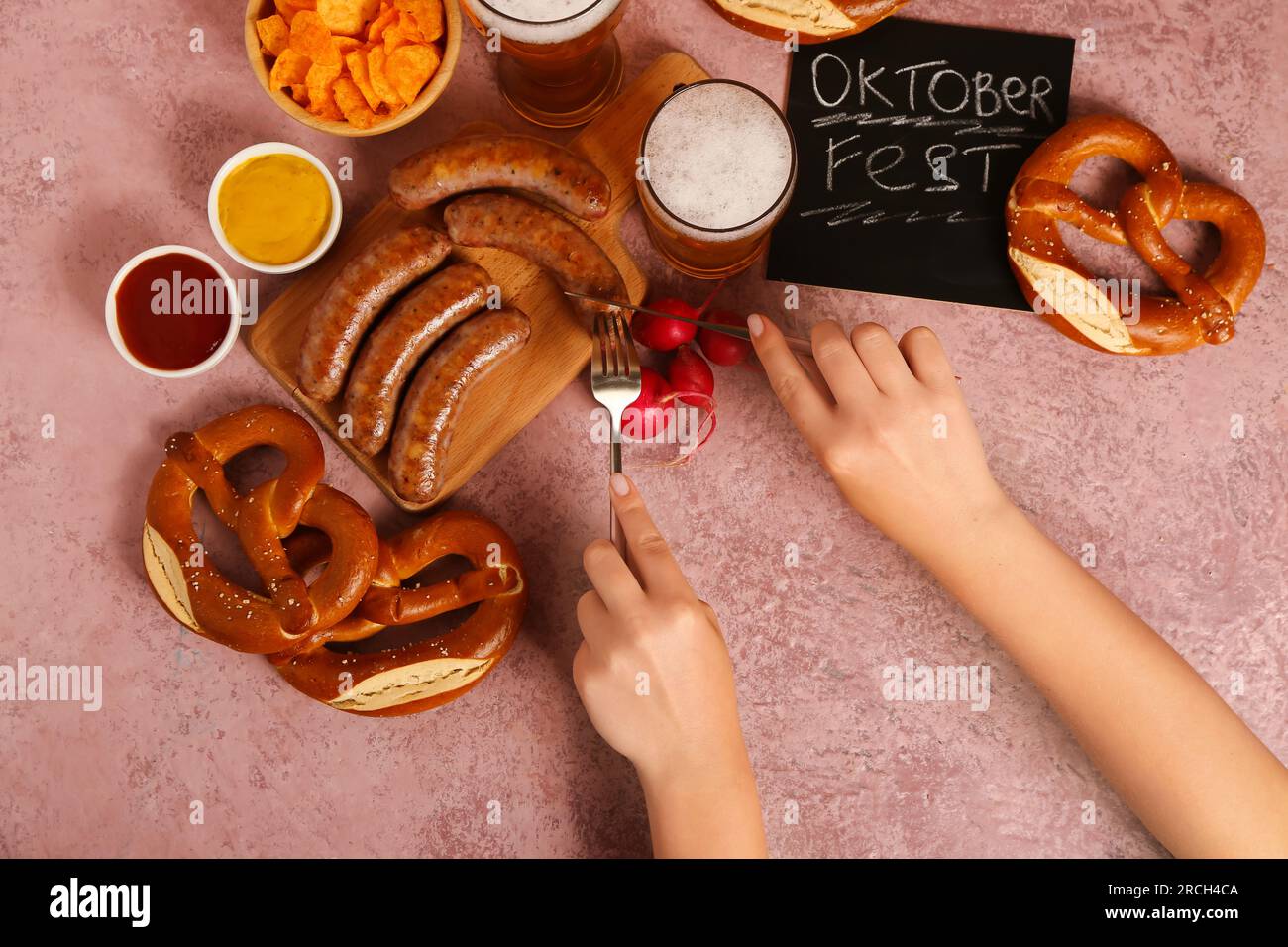 Femme mangeant de savoureuses saucisses bavaroises sur fond rose. Célébration de l'Oktoberfest Banque D'Images