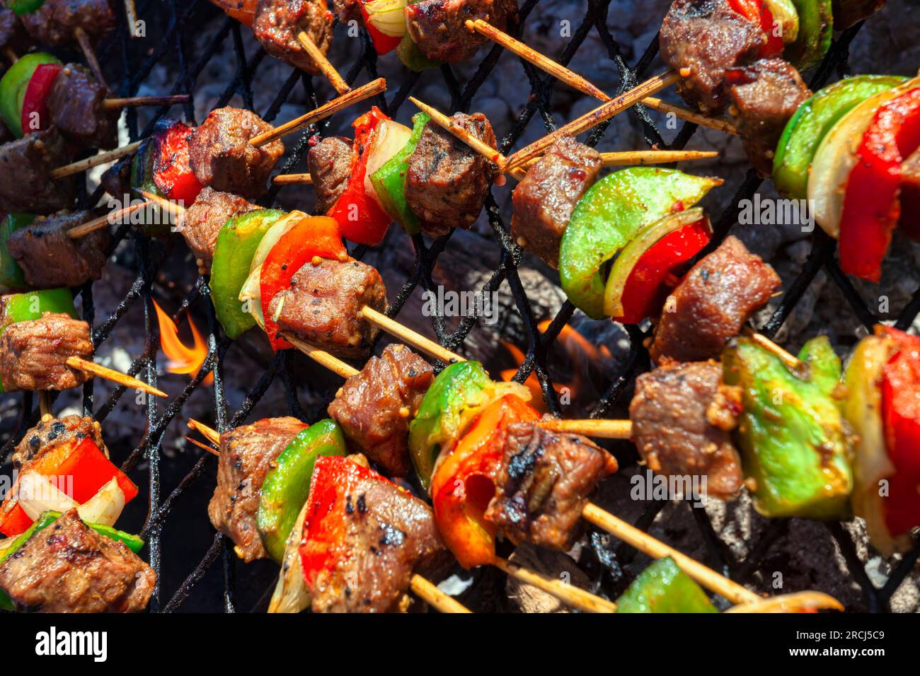 barbecue en plein air, petites flammes sur des brochettes de bois de kebab avec des poivrons de viande rouge et des oignons Banque D'Images