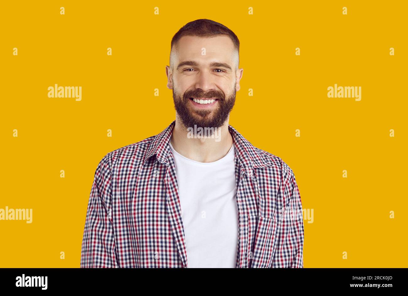 Portrait d'homme brunet souriant heureux dans une chemise à carreaux rouge sur fond jaune regardant la caméra. Banque D'Images