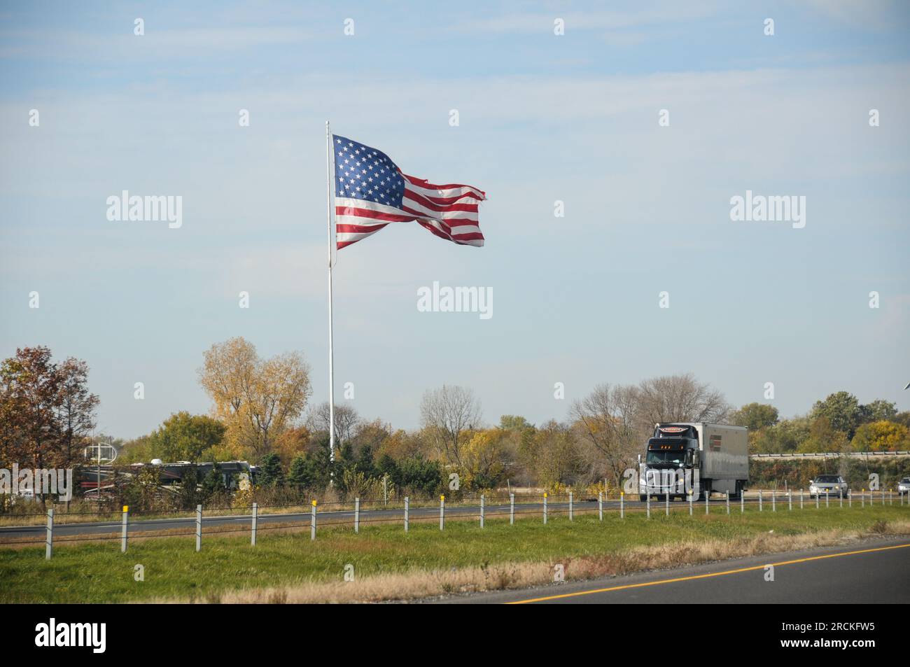 Chauffeur de camion américain dans une grosse plate-forme de 18 roues passant devant le drapeau des États-Unis sur la route de l'autoroute inter-états Banque D'Images