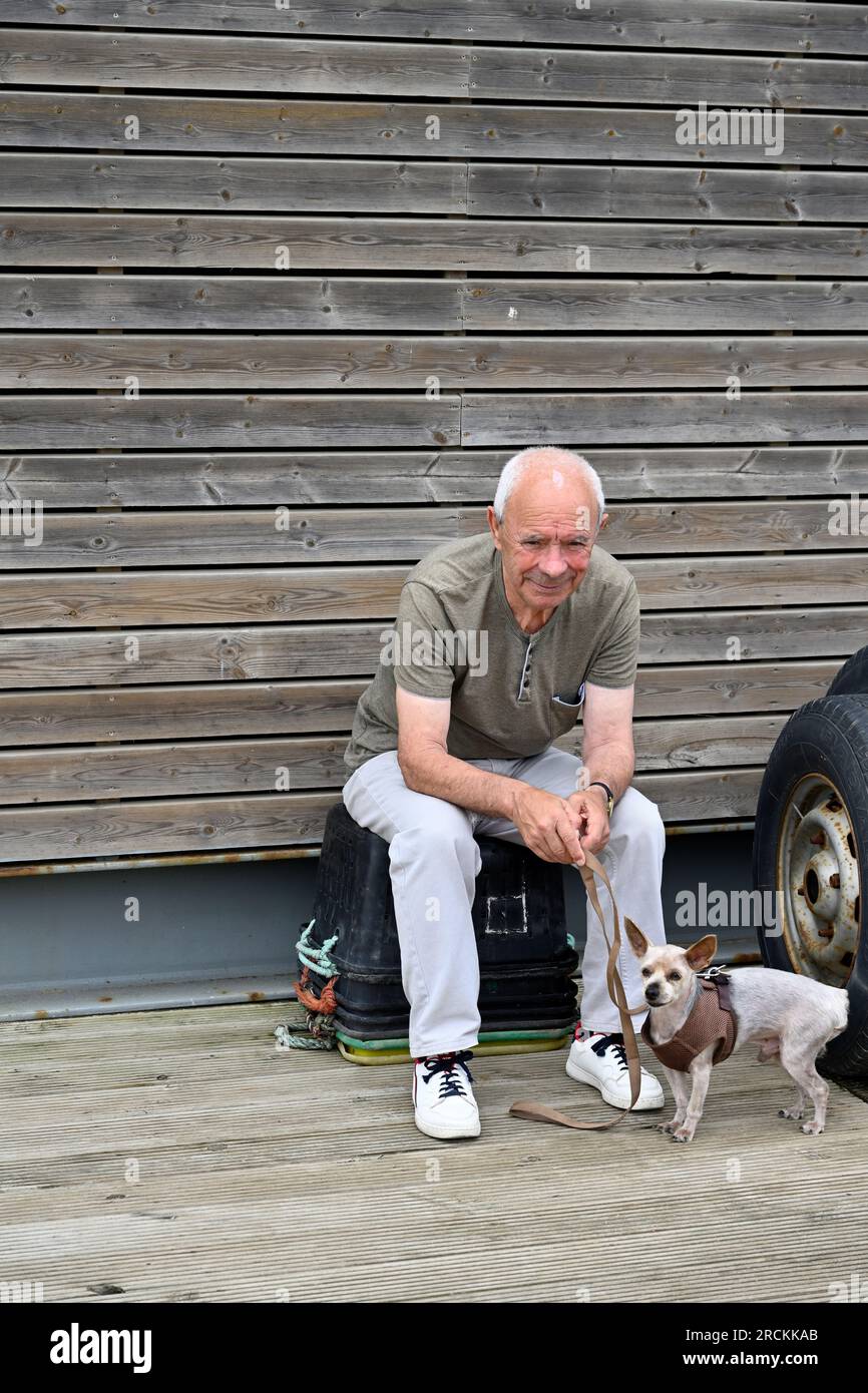 Homme portugais local plus âgé assis sur des baignoires retournées avec son chien, Praia do Bairro Piscatório, Portugal Banque D'Images