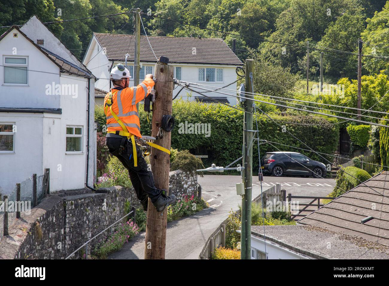 L'ingénieur OGI monte un poteau téléphonique installant un câble à fibre optique pour le haut débit à une maison résidentielle de village, pays de Galles, Royaume-Uni Banque D'Images