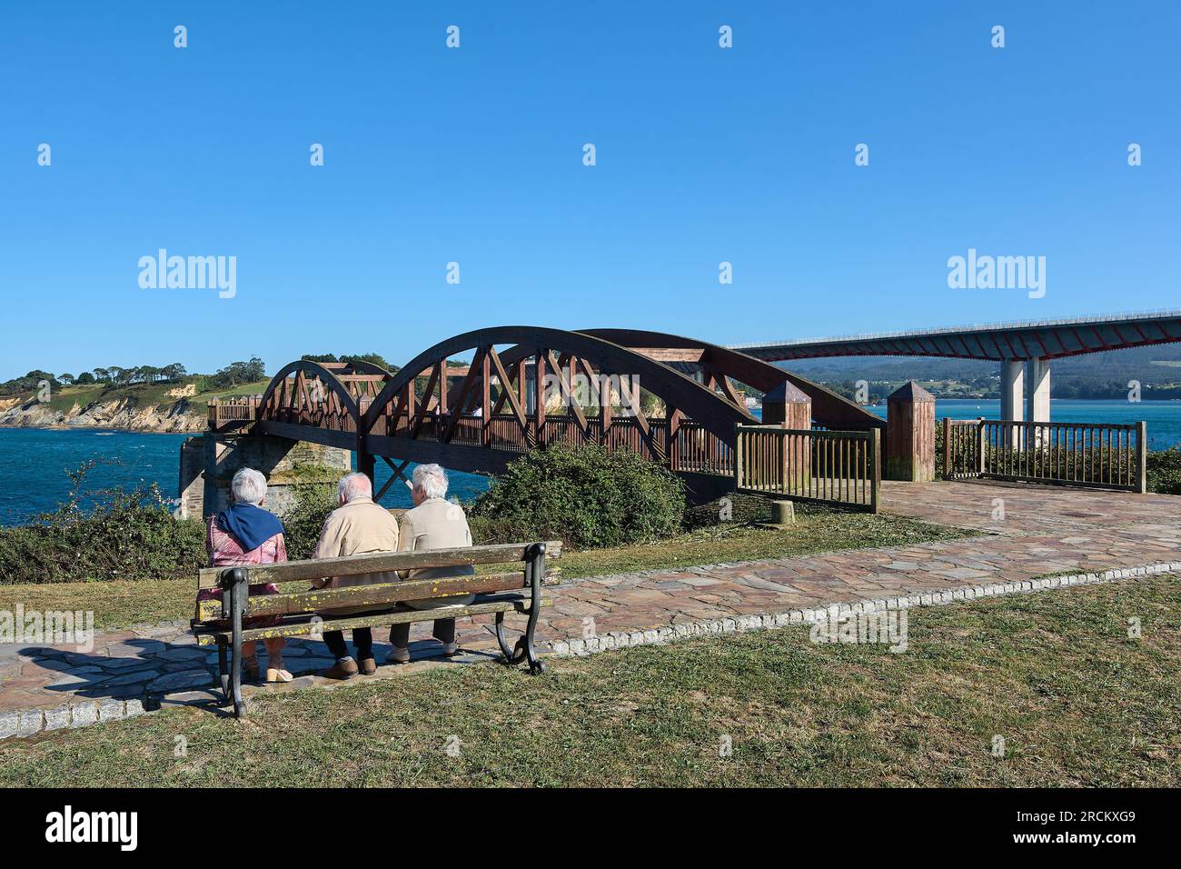 Personnes âgées méconnaissables assis sur un banc regardant le pont en bois sur les eaux de l'estuaire de Ribadeo Espagne Banque D'Images
