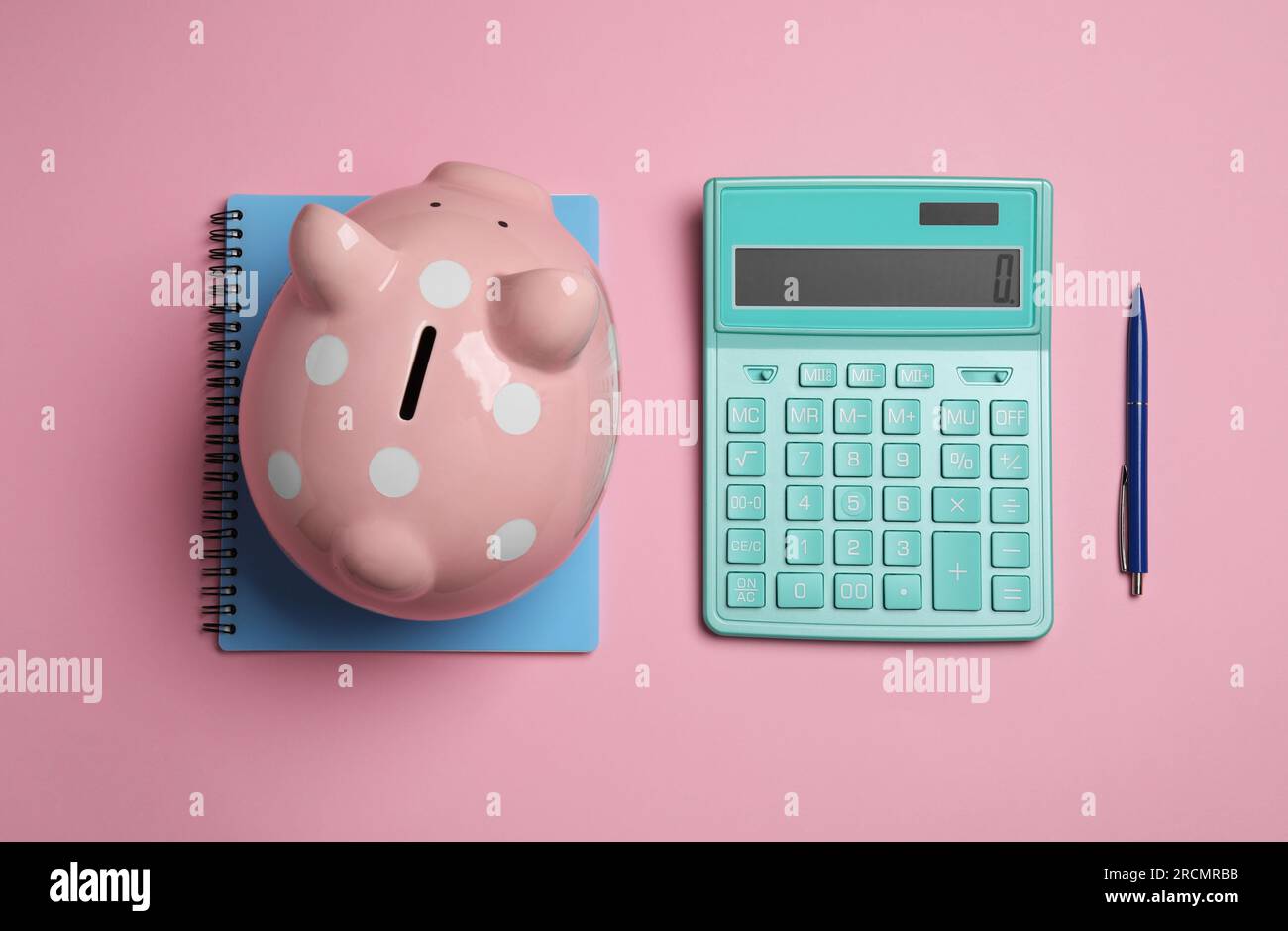 Calculatrice, tirelire, cahier et stylo sur fond rose, mise à plat Banque D'Images