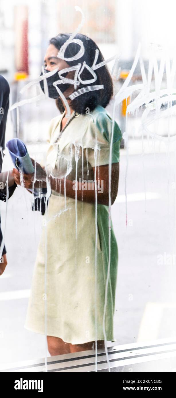 Dame asiatique debout à l'extérieur derrière le verre qui a l'écriture blanche sur le verre avec l'encre ou la peinture courant le long du verre. Banque D'Images