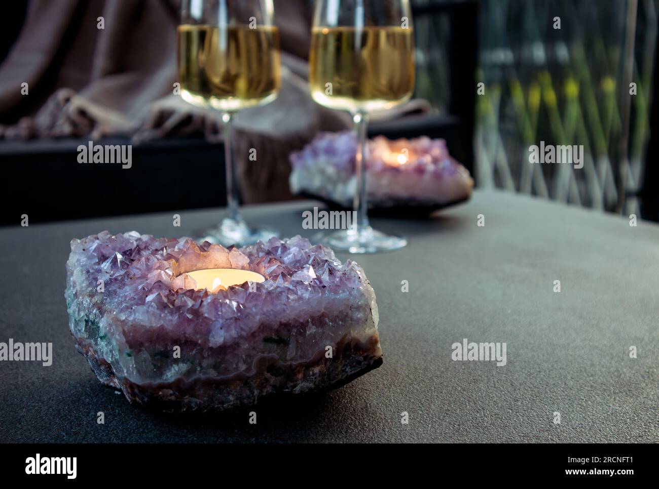 Focalisation sélective sur le support de bougie geode en cristal d'améthyste avec bougie chauffe-plat brûlant à l'intérieur, deux verres à vin blanc sur fond dans la soirée. Banque D'Images