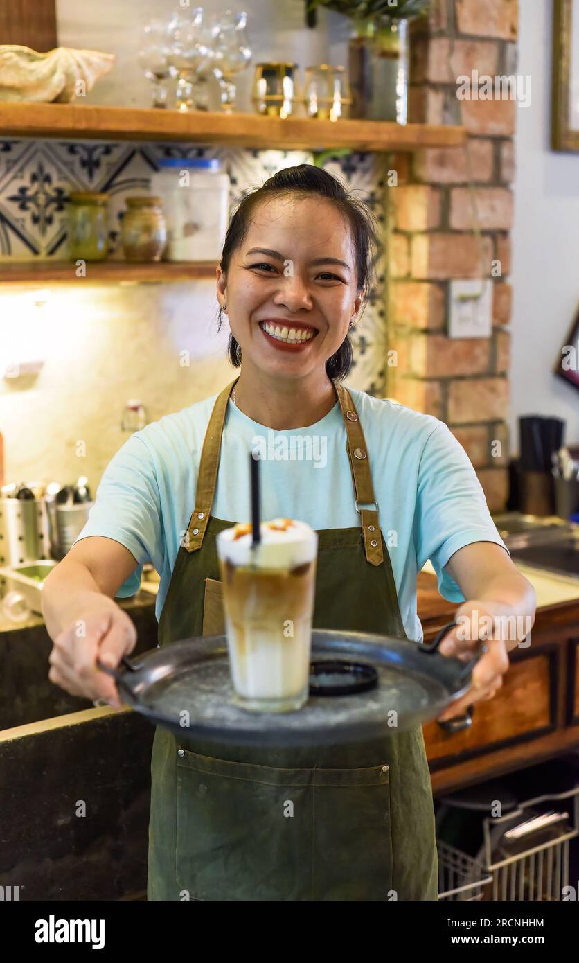 Serveuse vietnamienne tenant un verre de café glacé sur un plateau dans un café Banque D'Images