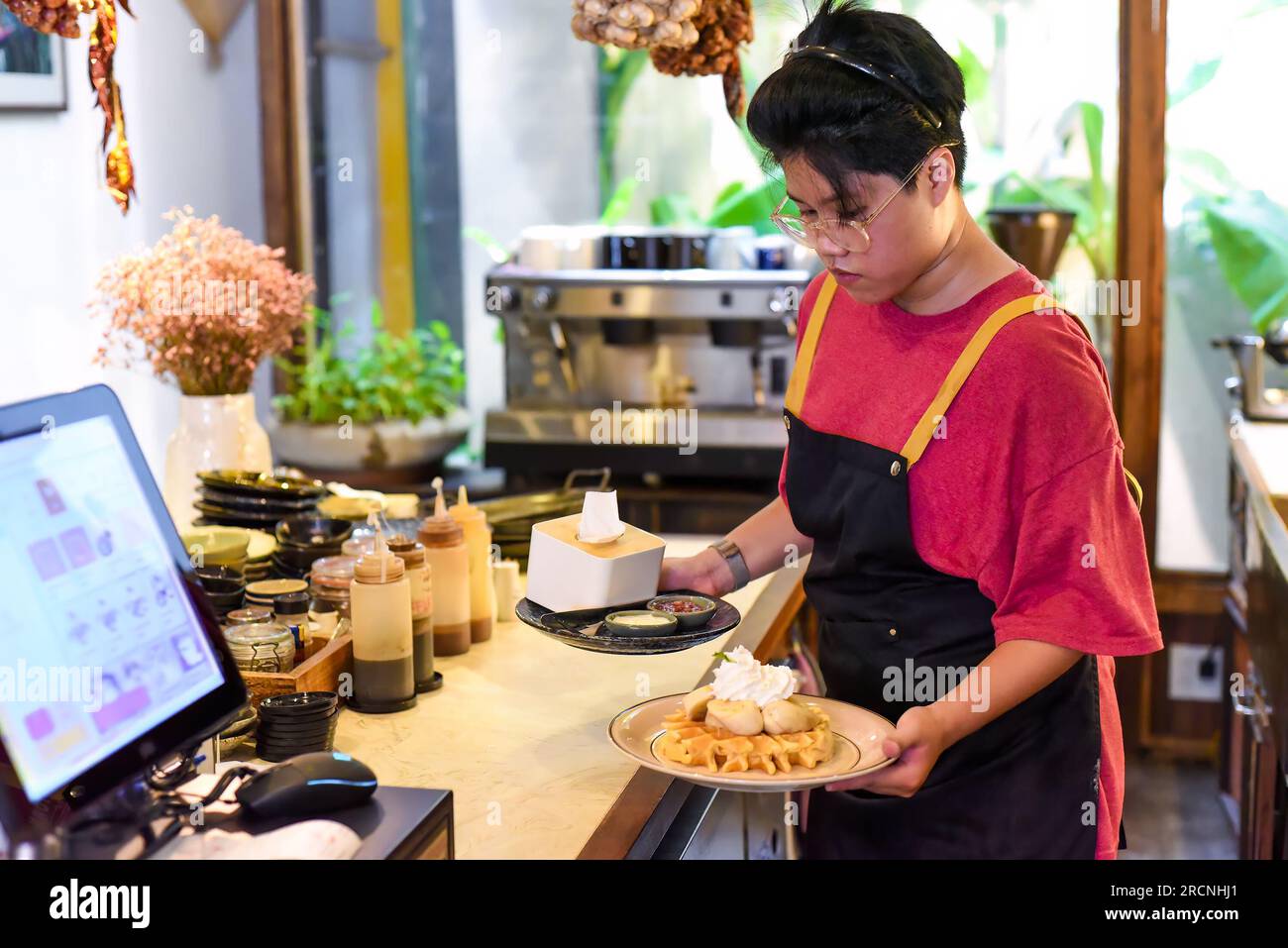 Jeune serveuse vietnamienne servant des gaufres sucrées avec de la banane et de la crème dans un café Banque D'Images