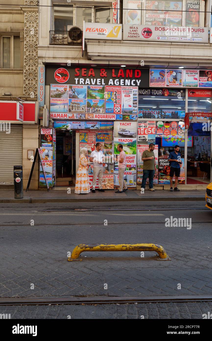 Groupe de personnes debout sur un trottoir devant une agence de voyages parlant et buvant un matin d'été à Istanbul, Turquie Banque D'Images