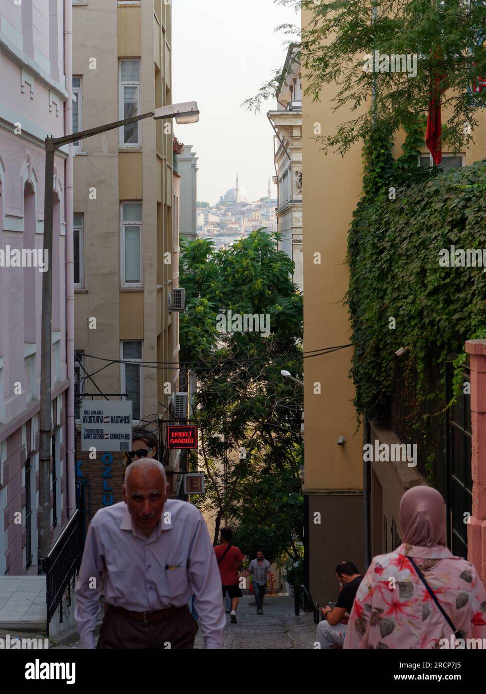 Les habitants marchent dans une rue étroite dans la région de Galata un soir d'été avec vue sur les mosquées au loin, Istanbul, Turquie Banque D'Images