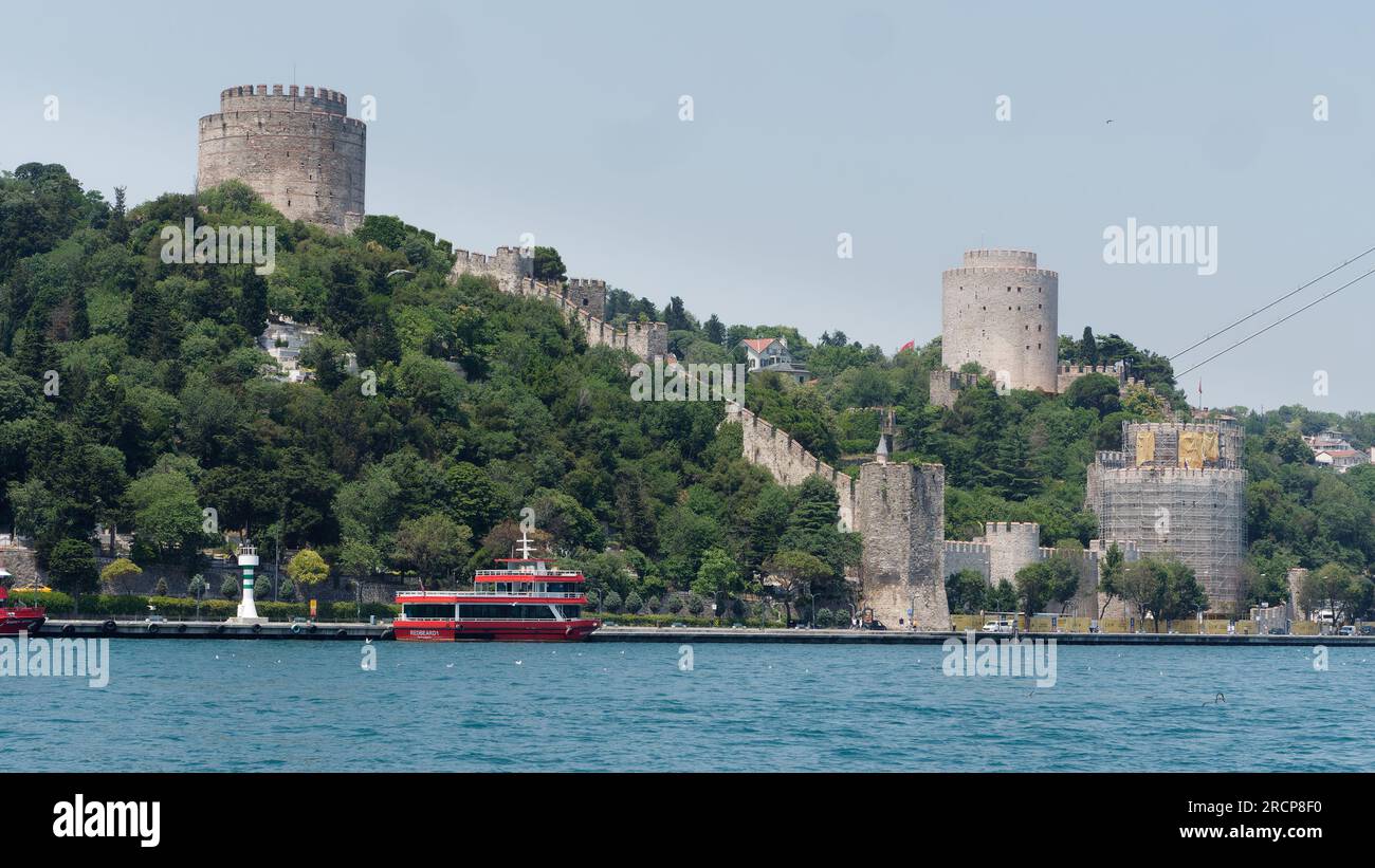 Forteresse Rumeli entourée d'arbres sur une colline sur les rives de la mer du Bosphore avec un ferry rouge à quai, Istanbul, Turquie Banque D'Images