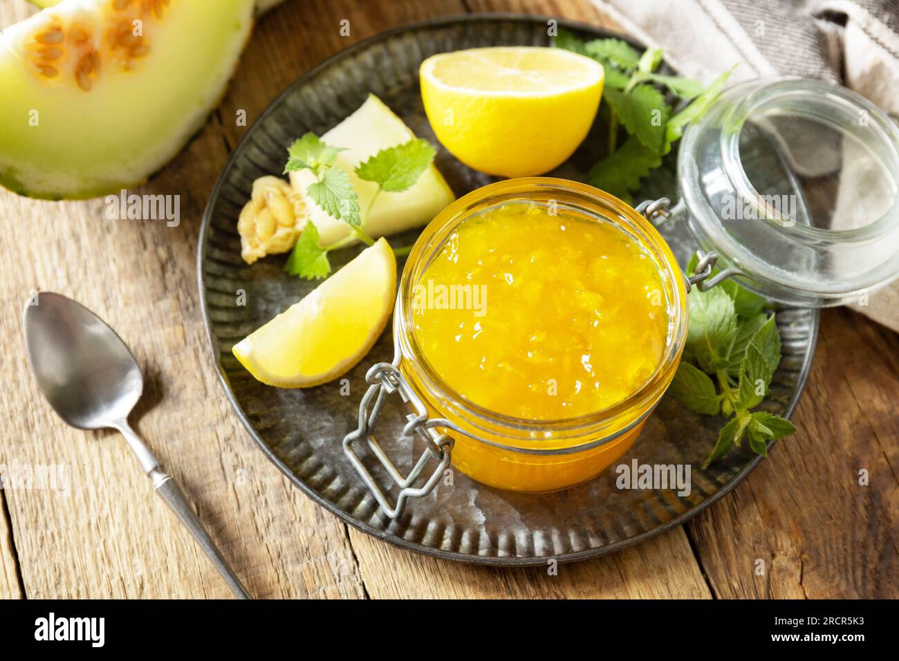 Conserves maison. Confiture de melon doux et d'agrumes ou gelée dans un petit bocal en verre avec des tranches de melon frais sur une table rustique en bois. Banque D'Images