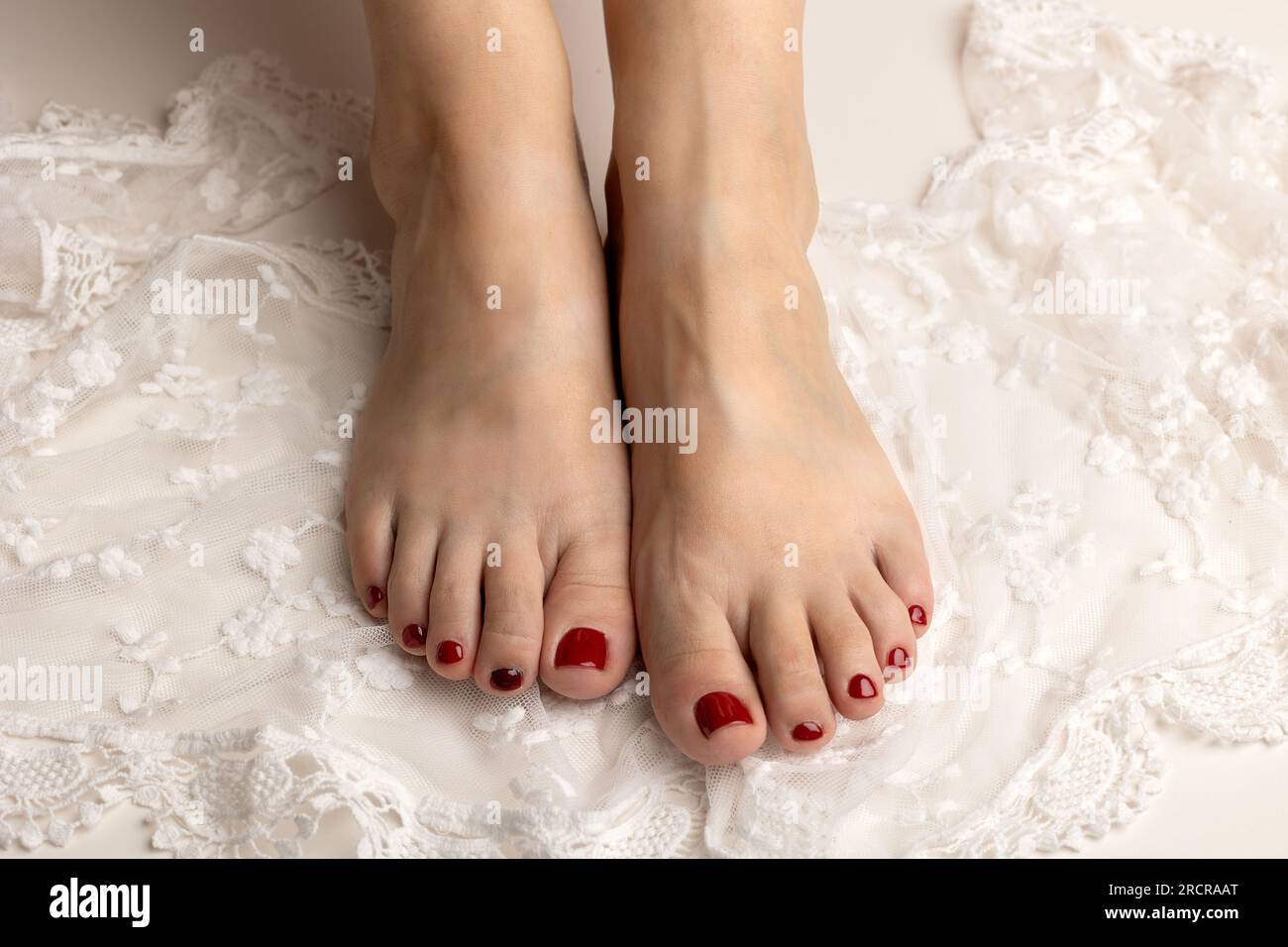 Gros plan de pieds féminins souples avec une belle pédicure rouge sur dentelle blanche Banque D'Images