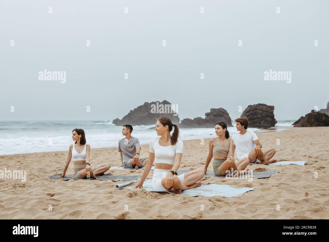 Entraînement de yoga d'été. Groupe d'hommes et de femmes pratiquant le yoga à la plage sur la rive de l'océan, assis sur des tapis de fitness Banque D'Images