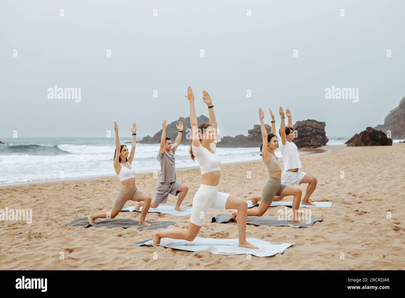 Équilibre pieds nus. Groupe de jeunes hommes et femmes pratiquant le yoga, méditant et faisant de l'exercice sur la plage le matin Banque D'Images