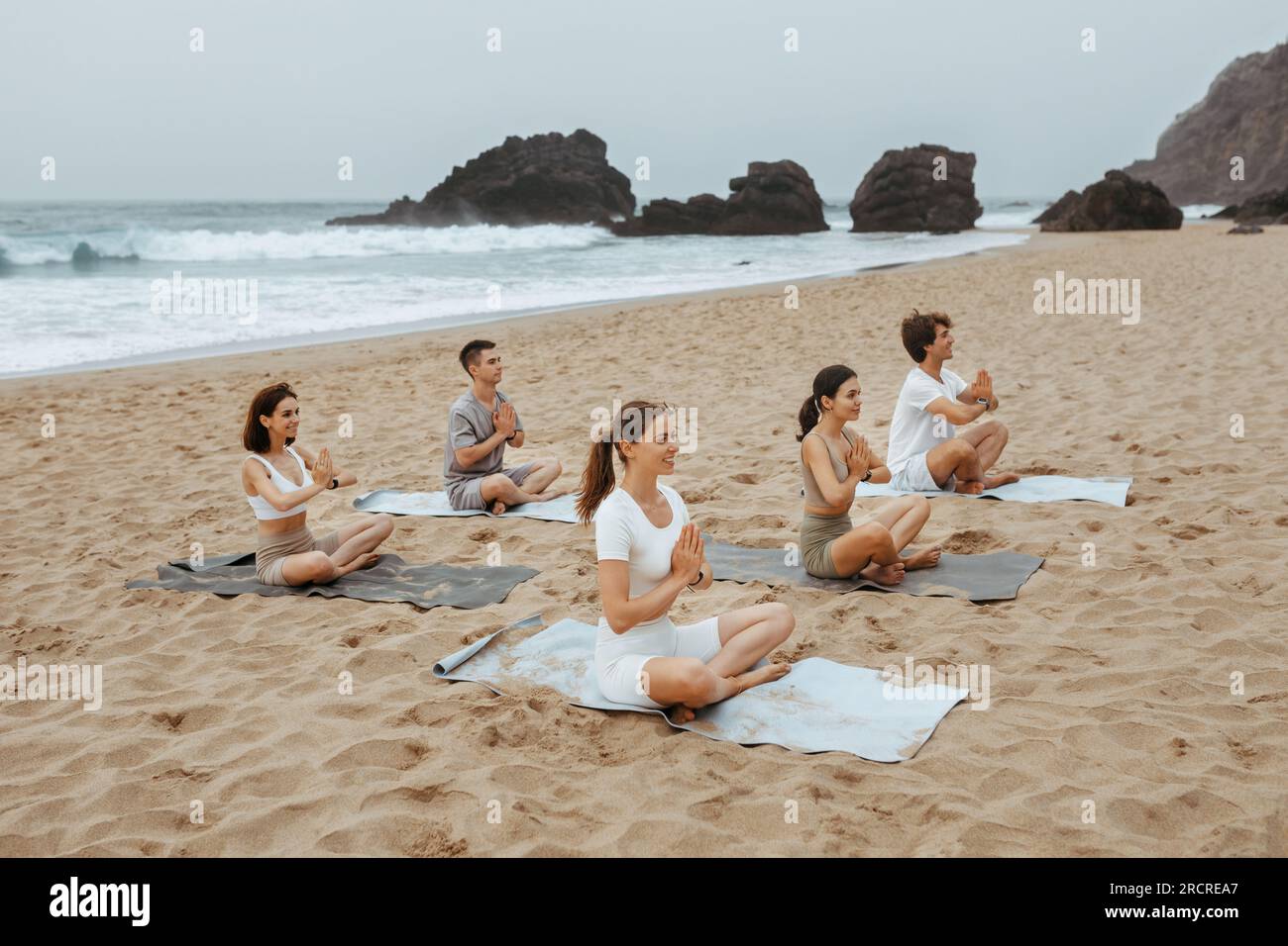 Formation de groupe. Des hommes et des femmes calmes enthousiastes méditant ensemble sur la plage de la rive de l'océan, pratiquant le yoga sur des tapis Banque D'Images