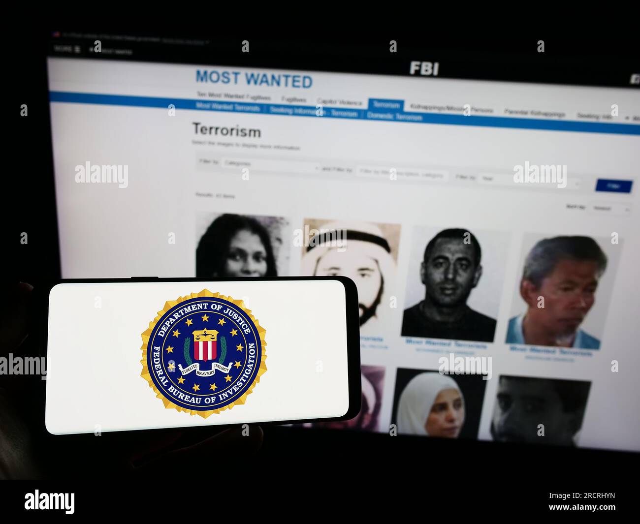 Personne tenant un téléphone portable avec sceau du Federal Bureau of Investigation (FBI) des États-Unis sur l'écran devant la page Web. Concentrez-vous sur l'affichage du téléphone. Banque D'Images
