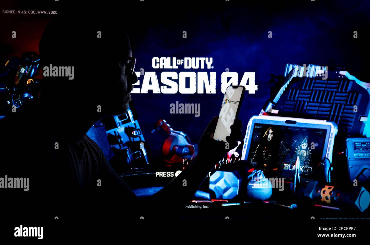 Le jeu Acitivision Call of Duty est vu en cours d'exécution sur une console PlayStation avec une personne tenant un appareil mobile au premier plan sur cette photo illu Banque D'Images