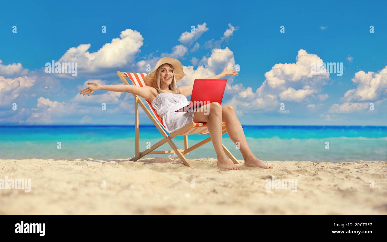 Jeune femme assise sur une chaise de plage avec un ordinateur portable et s'amusant Banque D'Images
