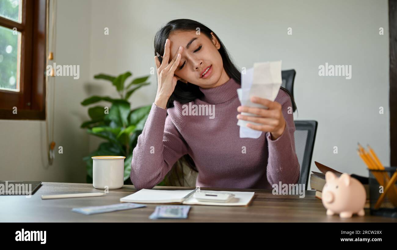 Une femme asiatique stressée et sérieuse assise à une table s'inquiétait de ses dépenses mensuelles tout en vérifiant ses factures d'électricité et en calculant son househo Banque D'Images