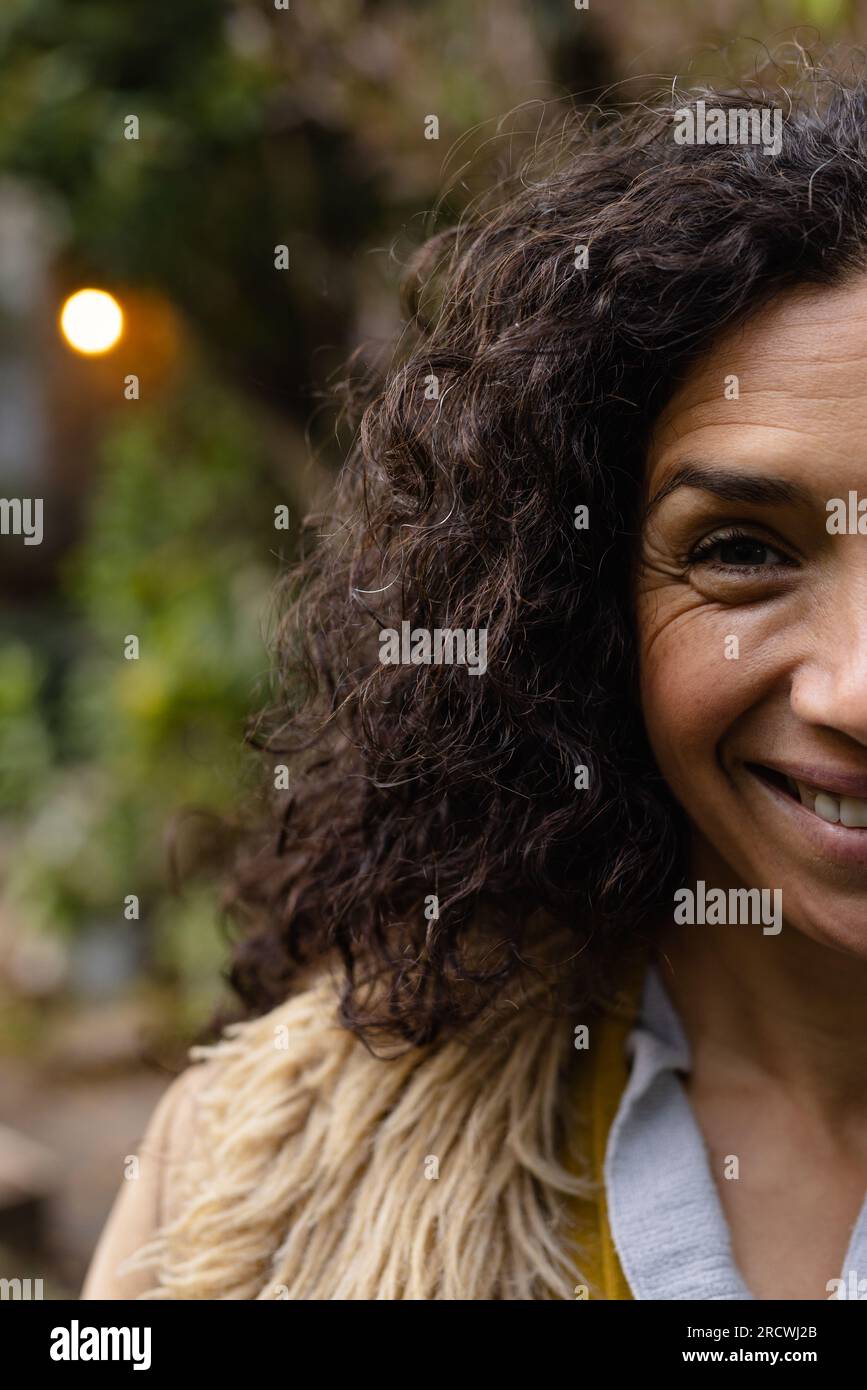 Portrait de femme biracial heureuse avec les cheveux bouclés foncés souriant dans le jardin Banque D'Images