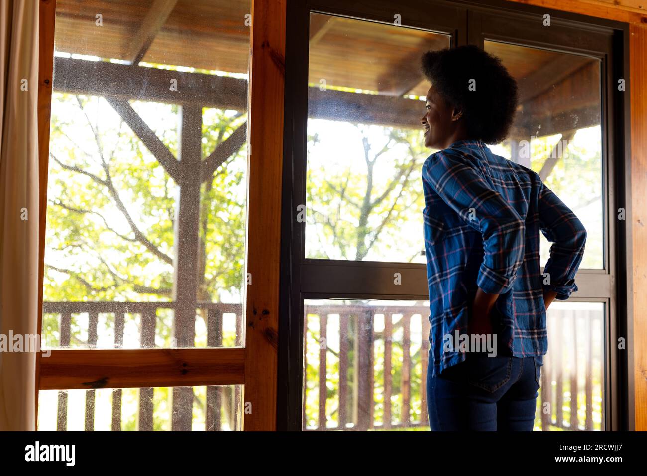 Heureuse femme afro-américaine dans le salon, regardant par la fenêtre au balcon ensoleillé, espace de copie Banque D'Images