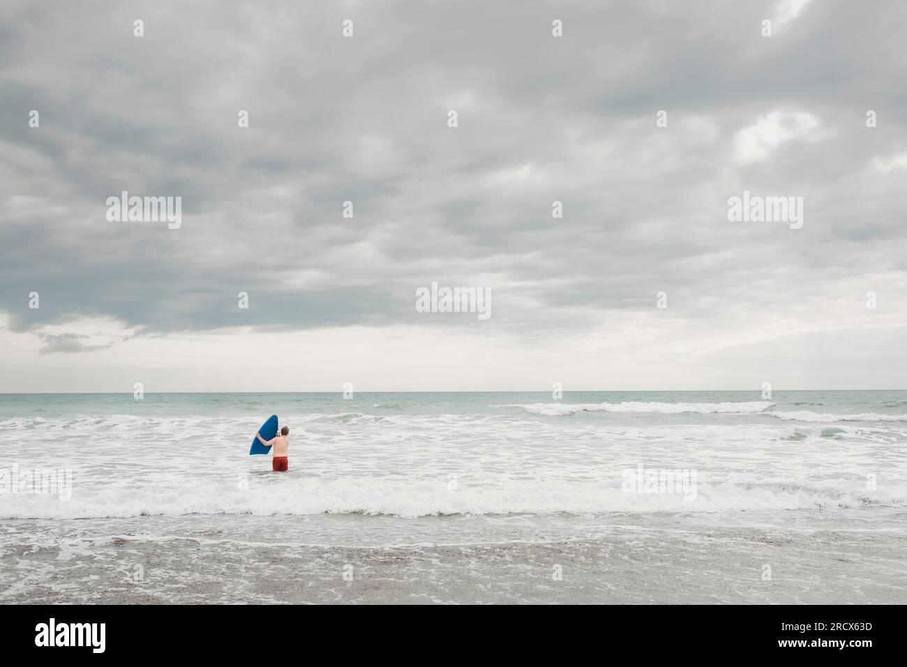 Jeune garçon avec planche de surf à la plage Banque D'Images