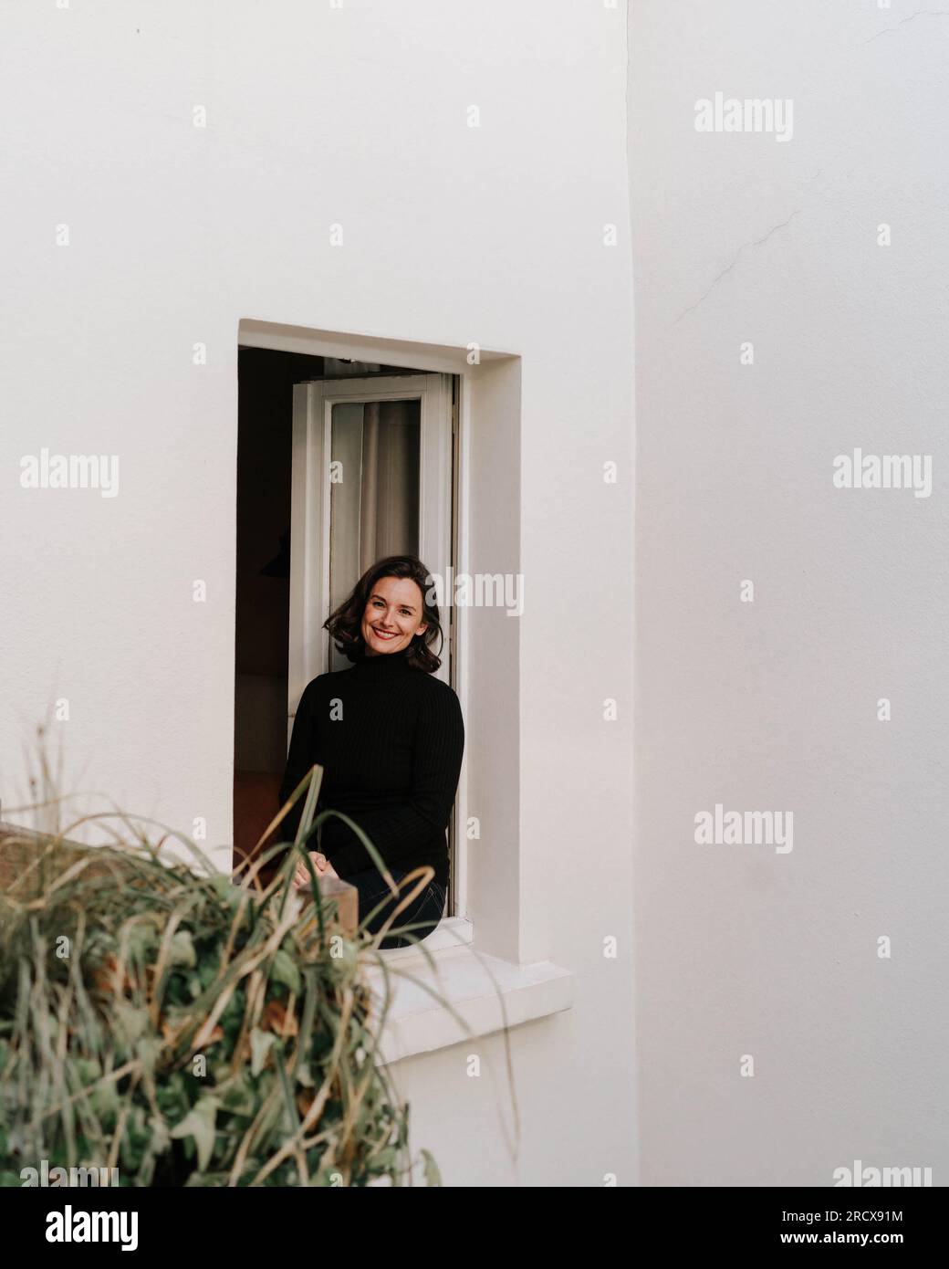 Femme élégante souriant à la caméra d'un cadre de fenêtre blanc Banque D'Images
