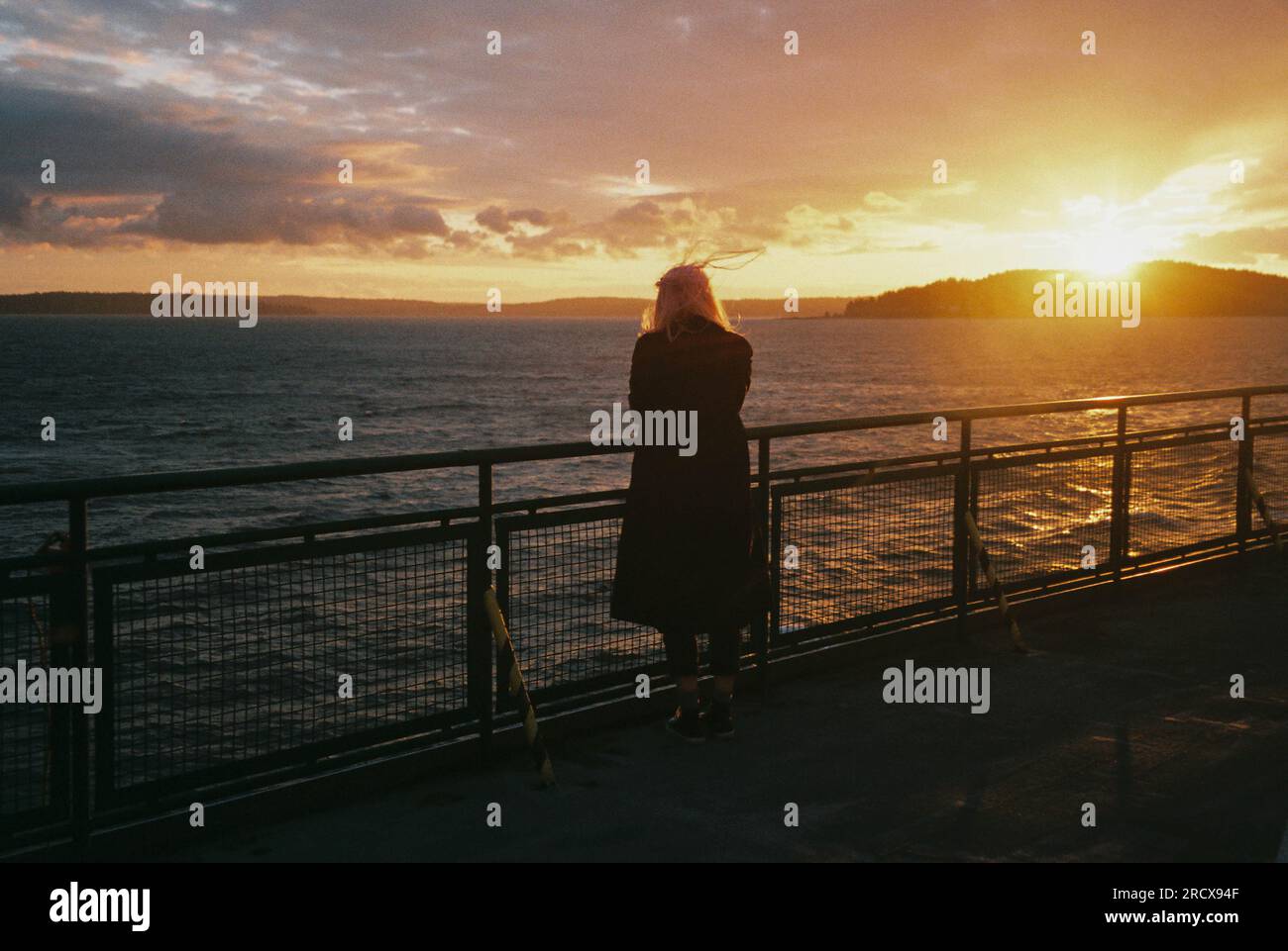 Silhouette femme avec les cheveux roses regarde le coucher du soleil de montagne sur le ferry. Banque D'Images