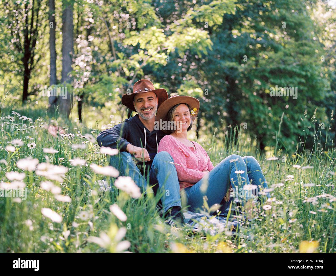 couple d'âge moyen assis ensemble dans l'herbe parmi les fleurs sauvages Banque D'Images