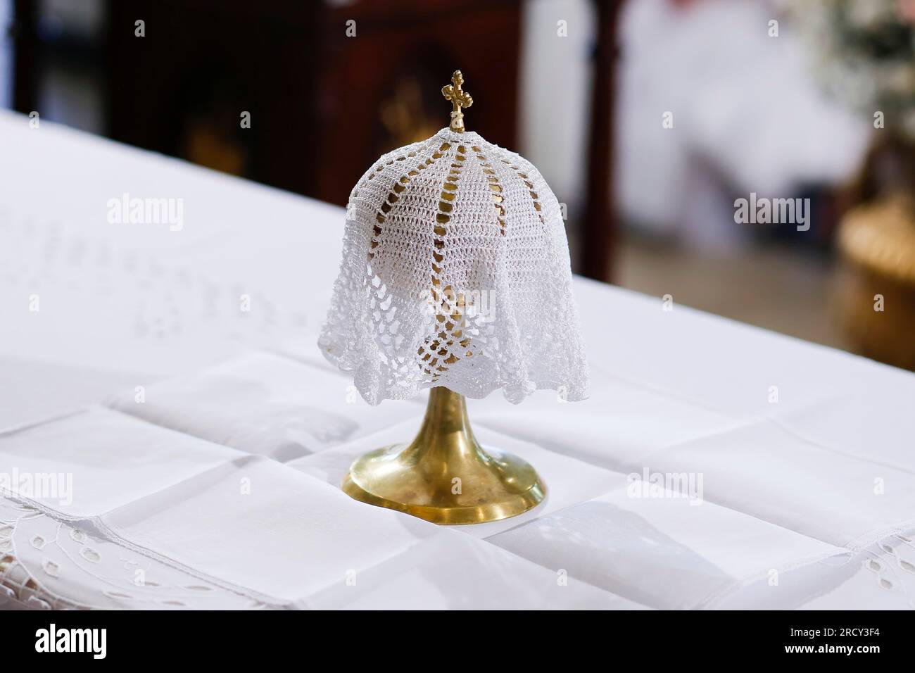 Calice ou gobelet en métal doré avec symbole de la croix du Christ, recouvert de tissu brodé blanc sur l'autel - ampoule Banque D'Images