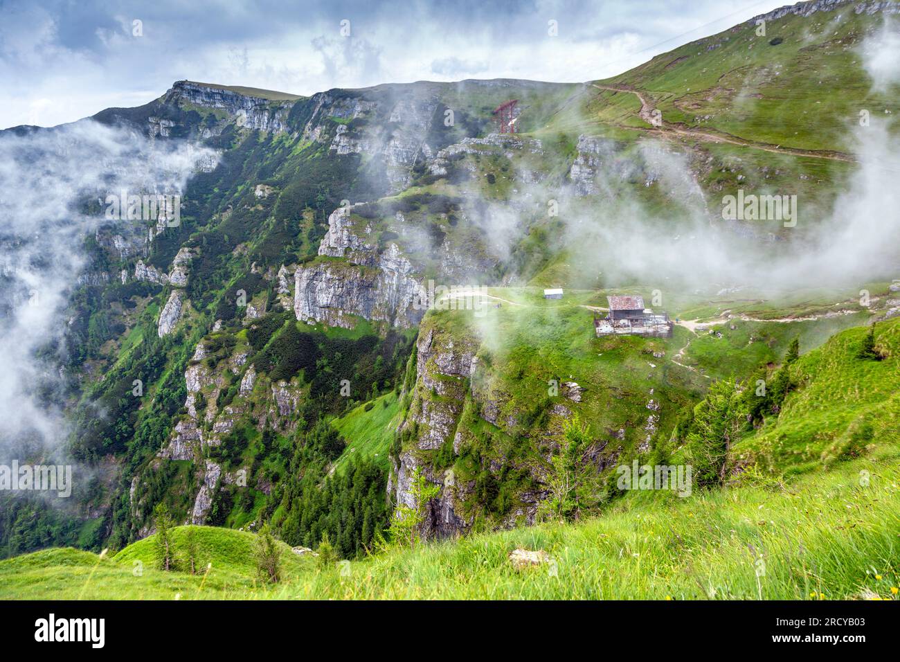 Cabane et montagnes enveloppées de nuages le long du chemin de randonnée de Busteni à Caraiman Peak dans les montagnes des Carpates, Roumanie. Banque D'Images