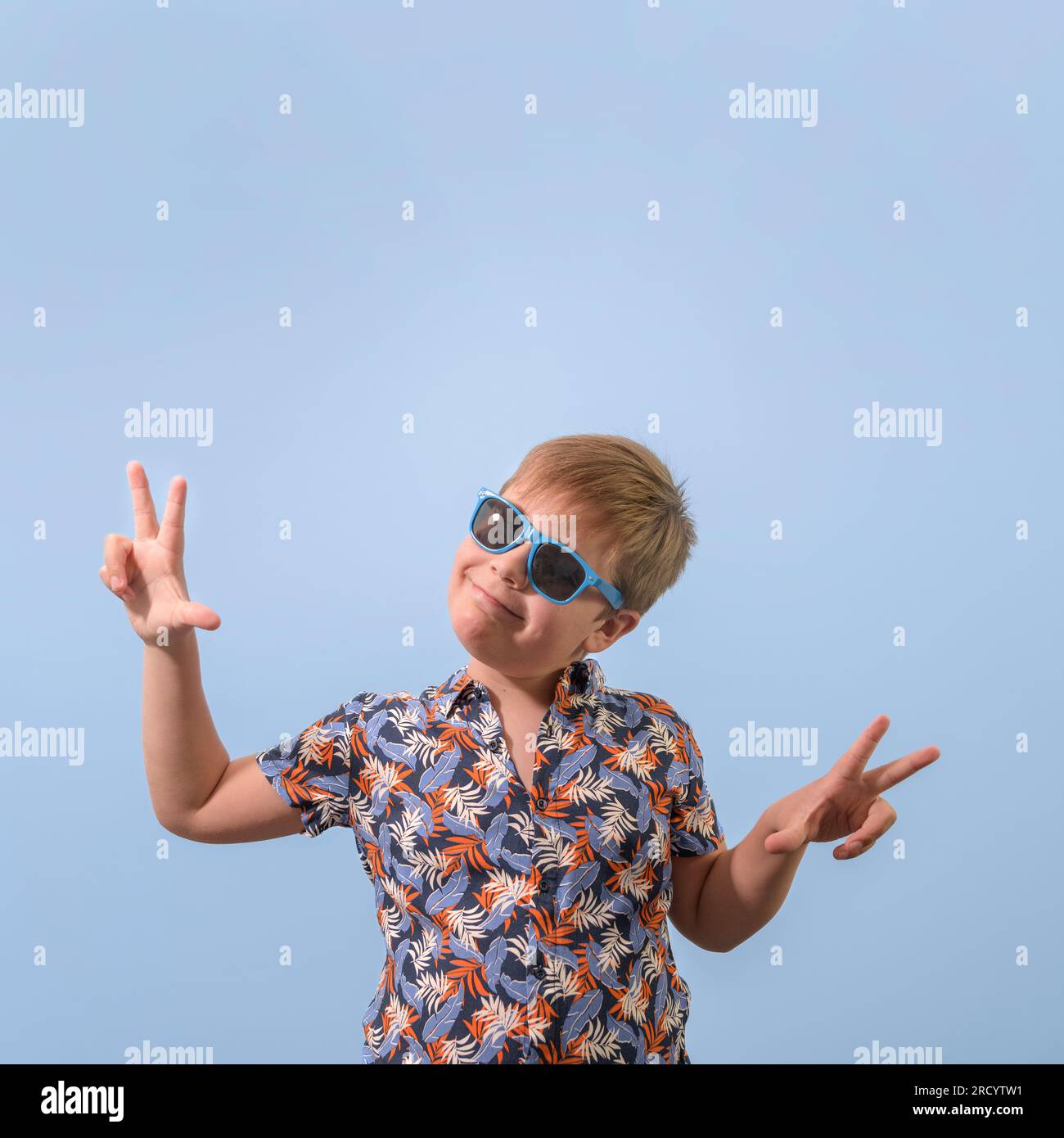 Un adolescent en chemise hawaïenne et lunettes de soleil. Les mains levées se réjouissent de rire de la caméra. Format carré Banque D'Images