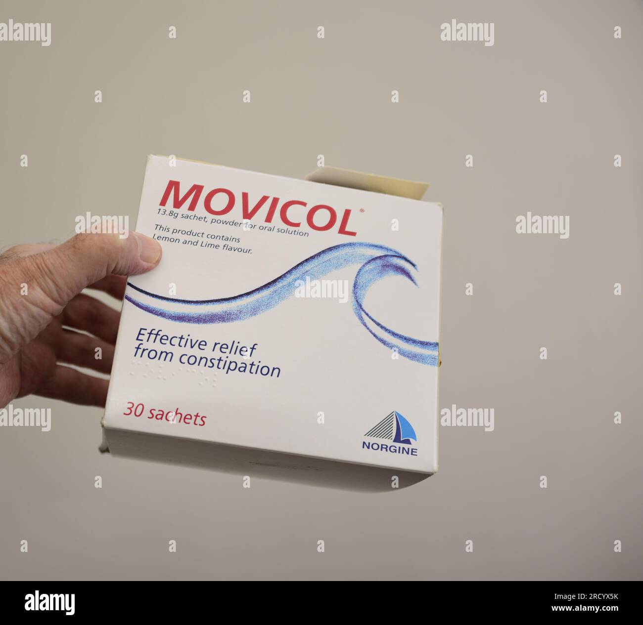 La main gauche d'un homme caucasien tient un paquet de Norgine marque ,30 Movicol sachets de 13,8 g, poudre pour solution buvable, soulagement efficace de la constipation Banque D'Images