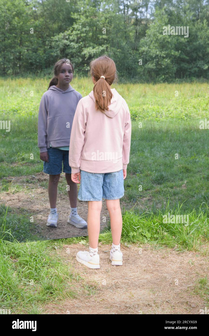 Nouvelle génération et nature - concept. Une adolescente sur une prairie verte se regarde dans le miroir. Banque D'Images