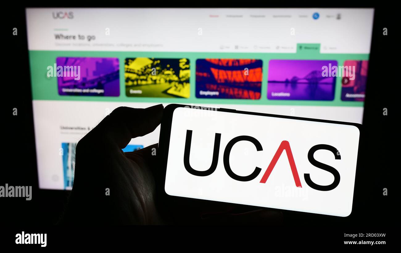 Personne tenant le téléphone mobile avec le logo du service des admissions des universités et collèges (UCAS) sur l'écran en face de la page Web. Concentrez-vous sur l'affichage du téléphone. Banque D'Images