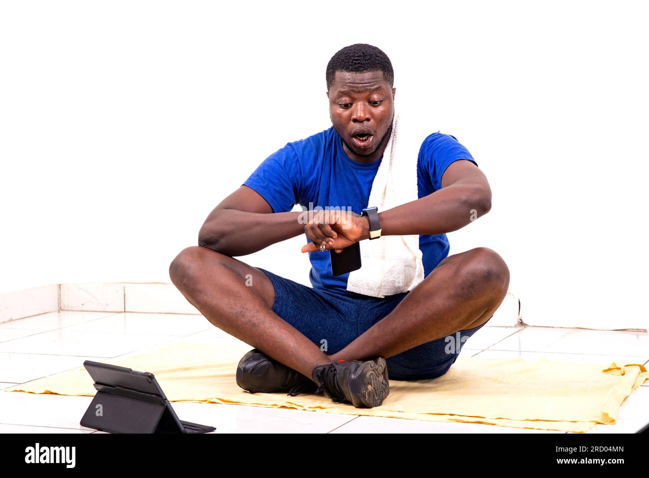 portrait d'un beau jeune sportif homme surpris assis sur le sol et regardant l'heure sur sa montre-bracelet. Banque D'Images