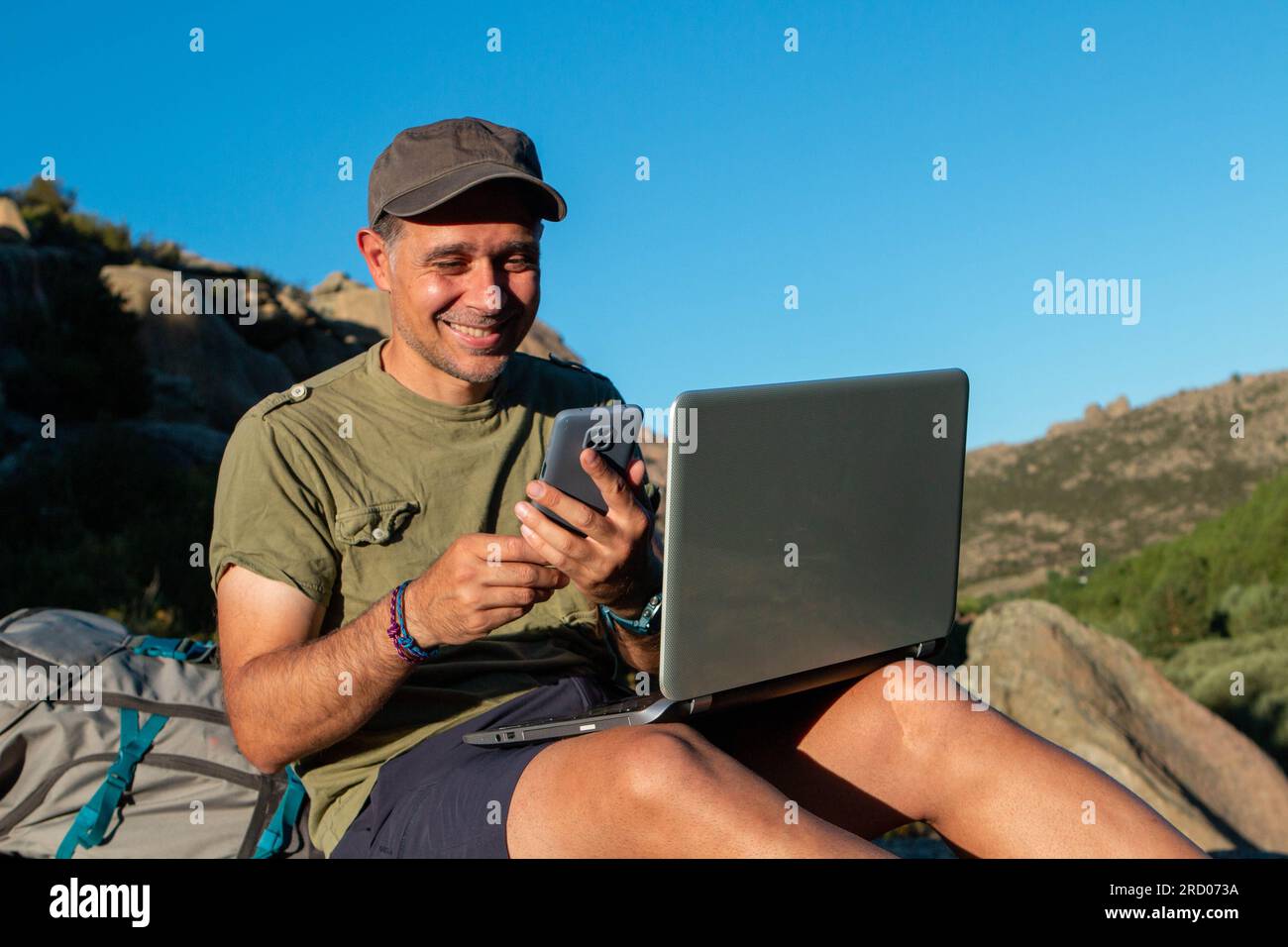 L'homme avec une casquette est allé à la montagne pour travailler avec un ordinateur portable et son téléphone portable Banque D'Images