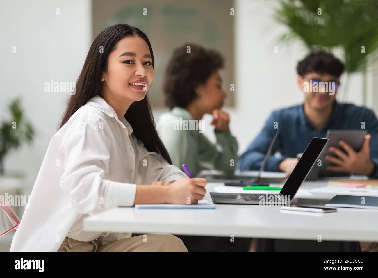 Asian Businesswoman Near Laptop assis au bureau avec des collègues à l'intérieur Banque D'Images