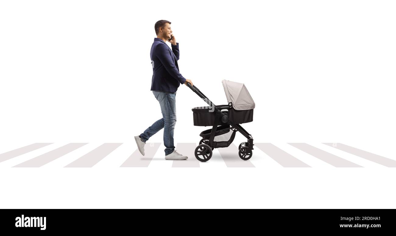 Photo de profil en longueur d'un père qui fait une poussette de bébé marchant et tapant sur un téléphone portable à un passage pour piétons isolé sur fond blanc Banque D'Images