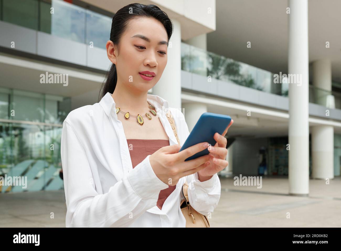 Femme d'affaires joyeuse lisant des messages texte de son collègue lorsqu'elle se tient debout à l'extérieur Banque D'Images