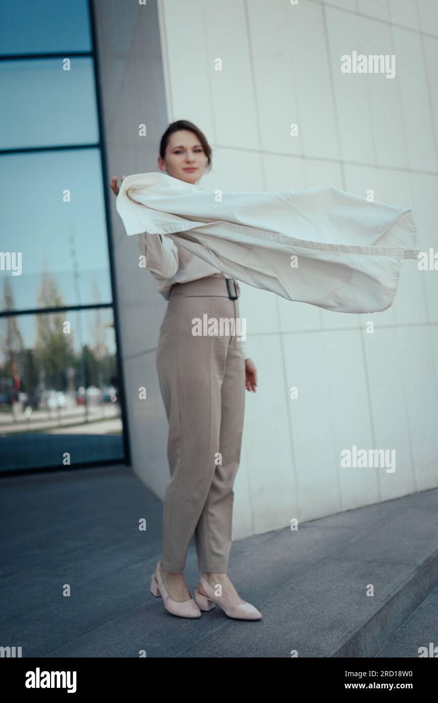 Portrait d'une femme d'affaires mignonne réussie dans un costume pantalon beige élégant debout près de l'immeuble de bureaux, vertical Banque D'Images