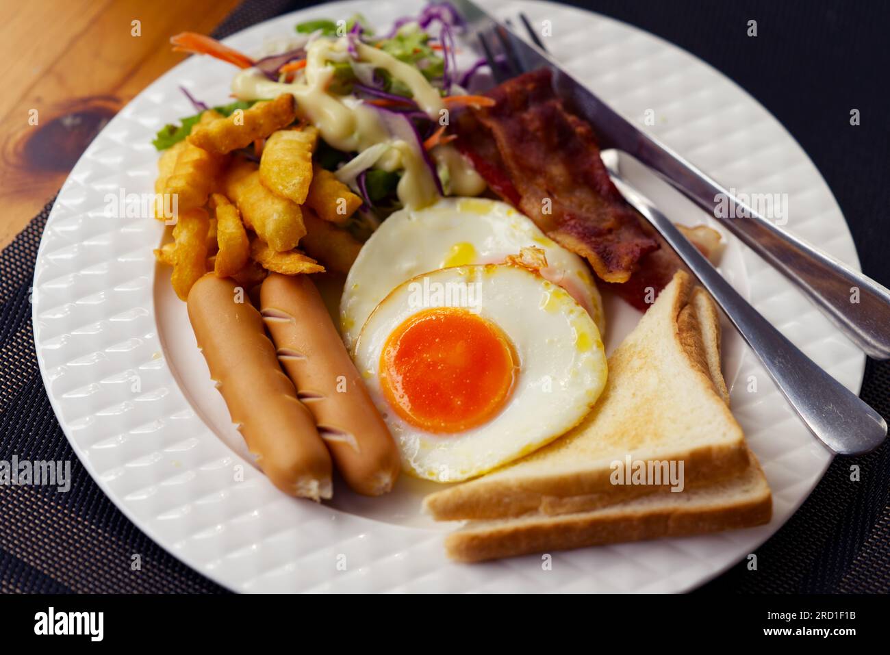 Petit déjeuner avec saucisses, œufs, pain, bacon, frites et salade fraîche dans un plat blanc sur une table en bois, image de nourriture en gros plan. Banque D'Images Petit déjeuner avec saucisses, œufs, pain, bacon, frites et salade fraîche dans un plat blanc sur une table en bois, image de nourriture en gros plan. Banque D'Images