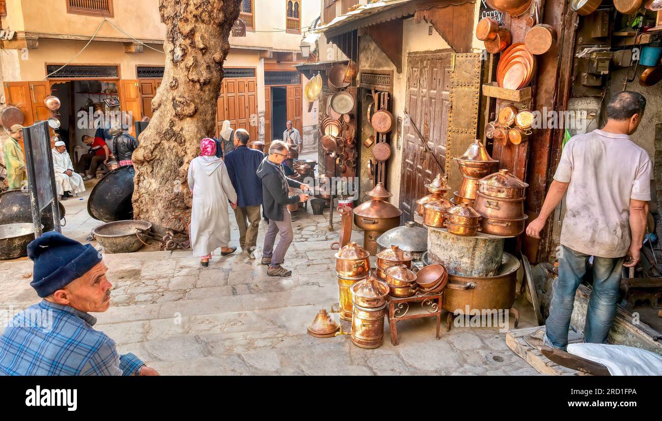 Fès, Maroc - 31 octobre 2015. La vie quotidienne dans le souk de la ville où les piétons marchent devant des expositions extérieures d'ustensiles de cuisine en cuivre. Banque D'Images