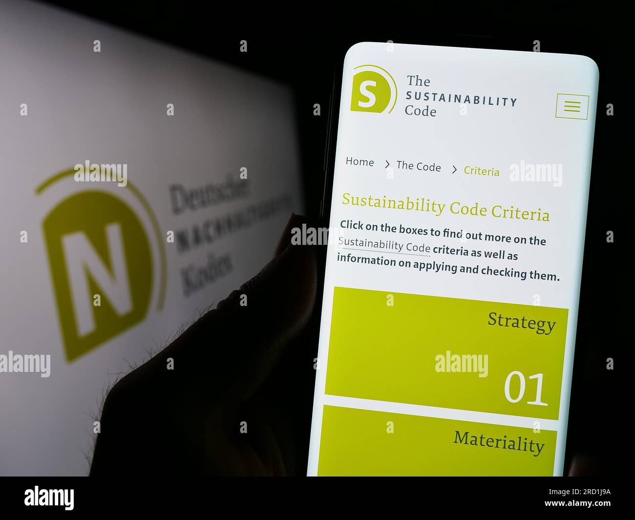 Personne tenant un téléphone portable avec la page web de Deutscher Nachhaltigkeitskodex (DNK) sur l'écran devant le logo. Concentrez-vous sur le centre de l'écran du téléphone. Banque D'Images