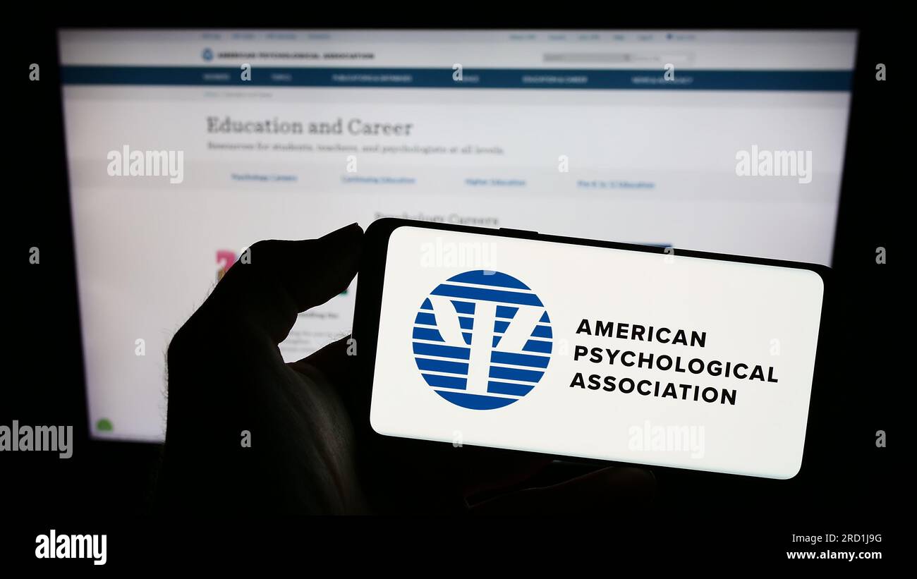 Personne tenant le téléphone portable avec le logo de l'American Psychological Association (APA) sur l'écran devant la page Web. Concentrez-vous sur l'affichage du téléphone. Banque D'Images