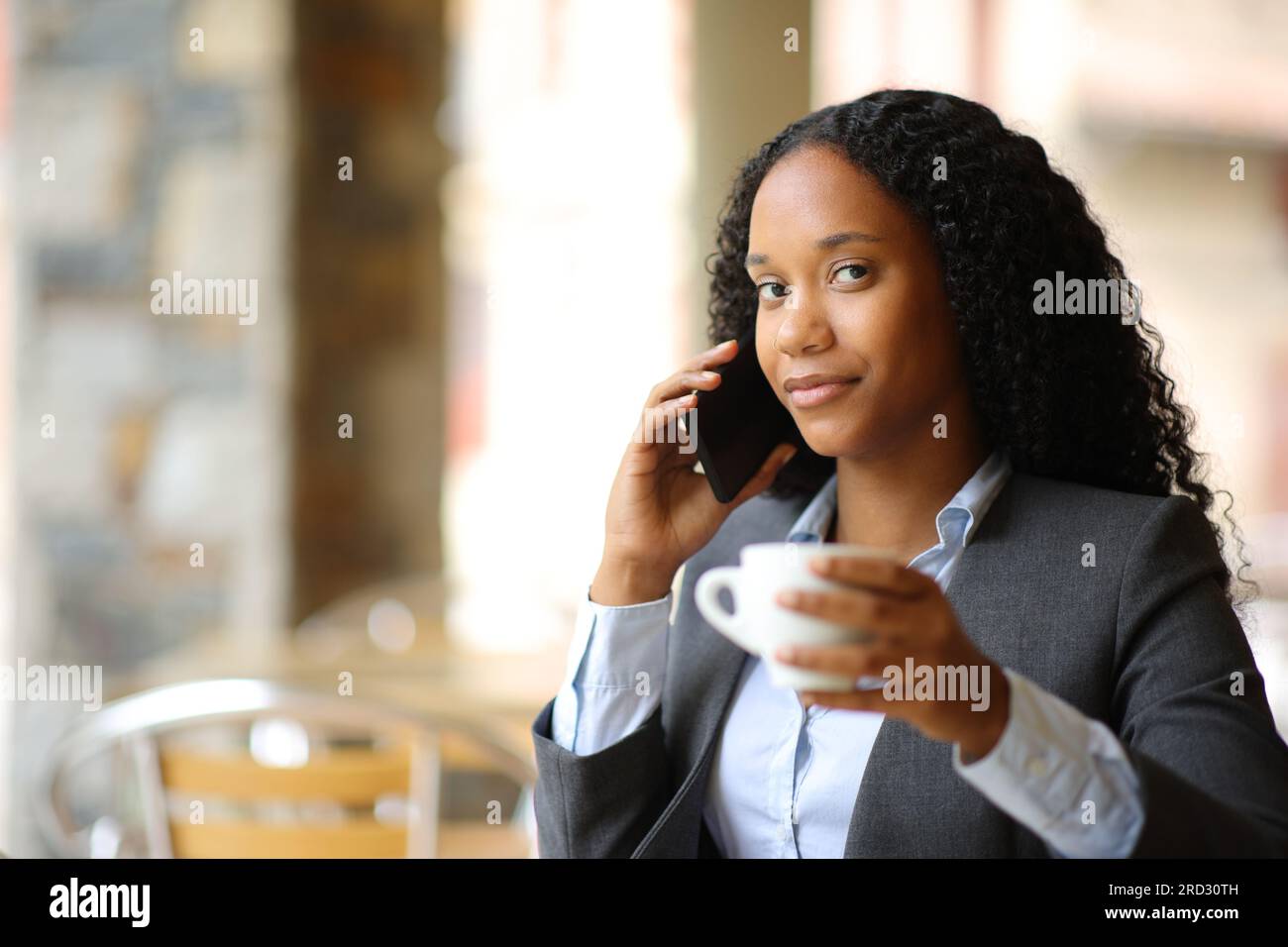 Femme d'affaires noire appelant au téléphone regardant la caméra dans une terrasse de bar Banque D'Images