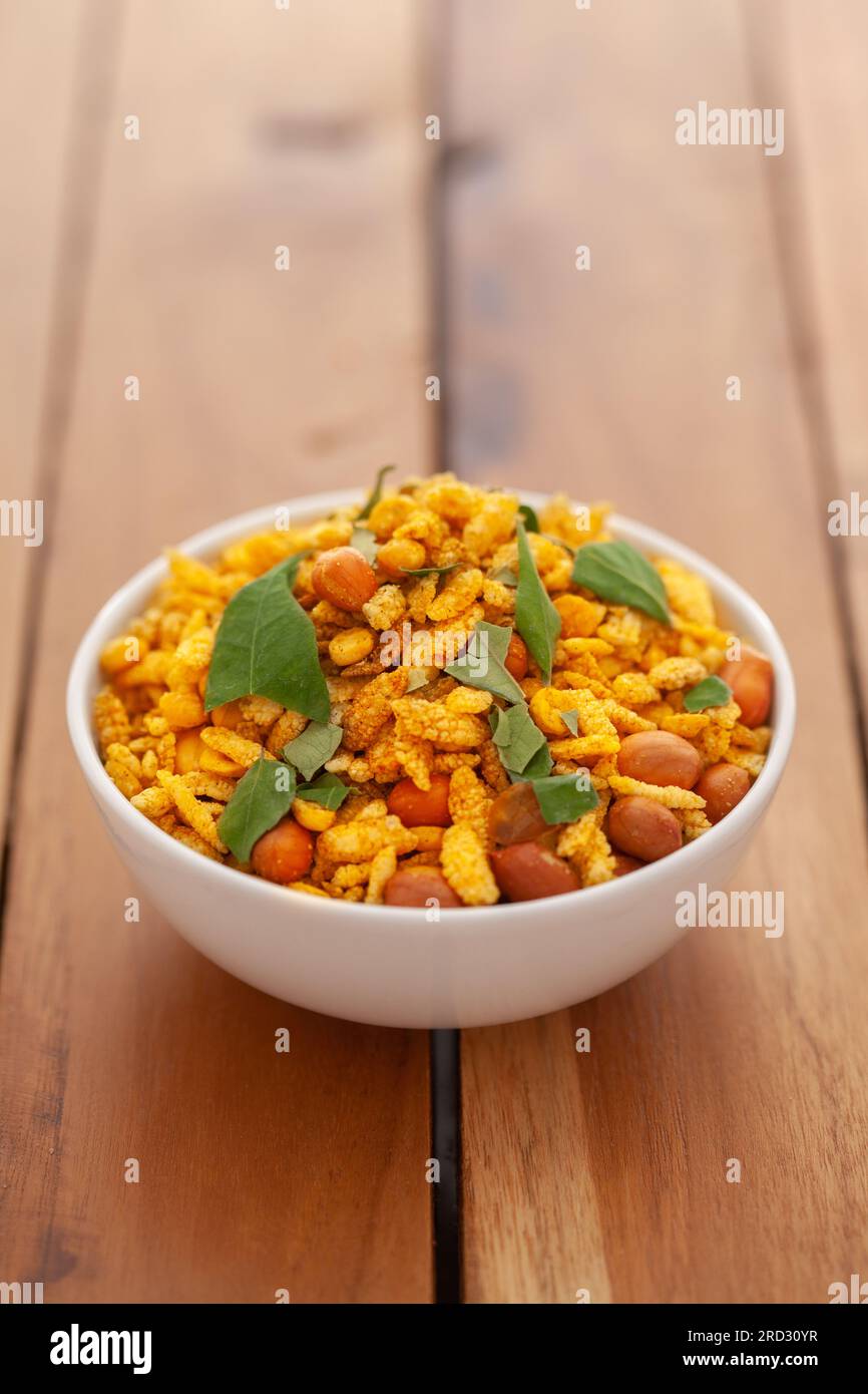Gros plan de cacahuètes salées mélangées de namkeen indien (collations) avec des feuilles de curry vert dans un bol en céramique blanche sur fond de bois Banque D'Images